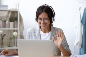 Smiling young Caucasian woman in headset wave greet talking on webcam virtual conversation on...
