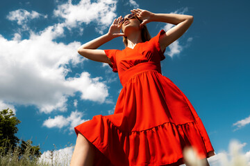 Model in a red dress on a blue background. Girl in a dress against the sky.