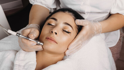 Obraz na płótnie Canvas Facial care procedure with apparatus to a brunette woman lying on the spa couch with closed eyes