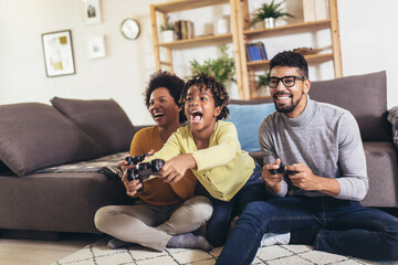 African American family at home sitting in sofa couch and playing console video games together - Powered by Adobe