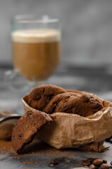 a cookie with pieces of chocolate tied with a string lies on a wooden board and next to a cup of latte
