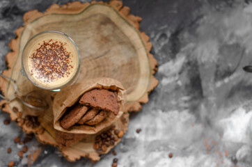 a cookie with pieces of chocolate tied with a string lies on a wooden board and next to a cup of latte
