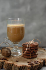 a cookie with pieces of chocolate tied with a string lies on a wooden board and next to a cup of latte