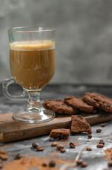 a cookie with pieces of chocolate tied with a string lies on a wooden board and next to a cup of latte