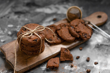 a cookie with pieces of chocolate tied with a string lies on a wooden board and next to a cup of latte