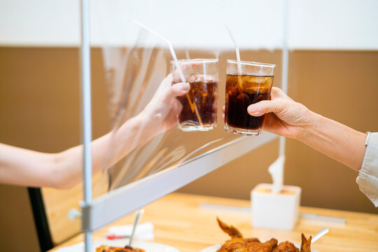 Asian Beautiful Female Clinking A Glass Of Water With Her Mother Who Siting Separate And Keep Distance With Table Plastic Shield Partition In Restaurant, New Normal And Social Distancing Concept