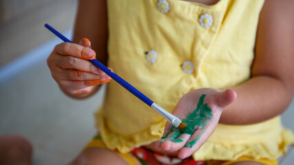 Kid paint her hands with brushes.