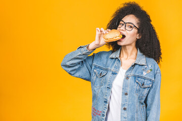 African American black young woman eating hamburger isolated on yellow background.