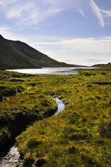Petit lac de montagne en Irlande se déversant un un fin ruisseau se transformant en rivière et se jetant dans la mer en contrebas.