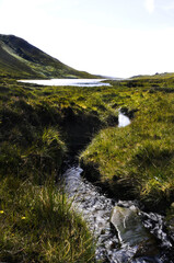 Petit lac de montagne en Irlande se déversant un un fin ruisseau se transformant en rivière et se...