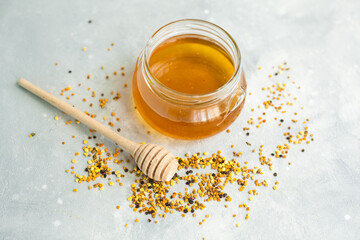 Obraz na płótnie Canvas Honey and honey spoon on a light background. Sweet honey in a jar, pollen scattered near the jar. Place for text 