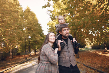 Fototapeta premium Family in a autumn park. Woman in a brown dress. Cute little girl with parents
