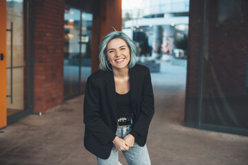 Laughing at camera caucasian woman with blue hair is posing outside in the street