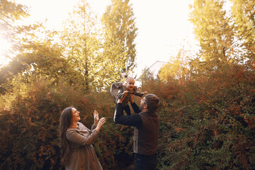 Family in a autumn park. Woman in a brown dress. Cute little girl with parents