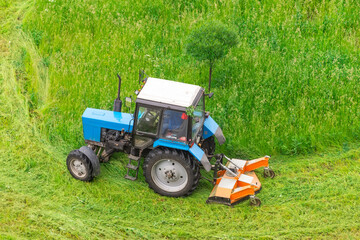 Tractor uses trailed lawn mower to mow grass on city lawns, aerial view.