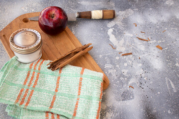 red apple, cinnamon stick and sugar on a wooden board and a knife with rustic background