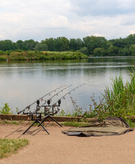Three fishing rods with reels at the side of a peaceful lake