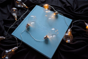 Blue wedding photo book with the inscription "wediing day" on a black fabric background. Around laid out retro garland.