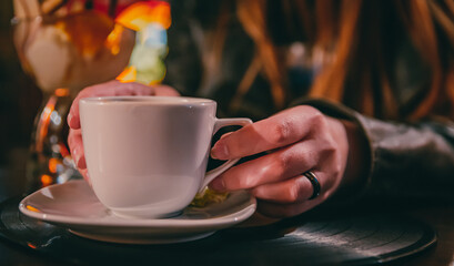 woman hands holding a white cup of tea or coffee standing on the table in cafe