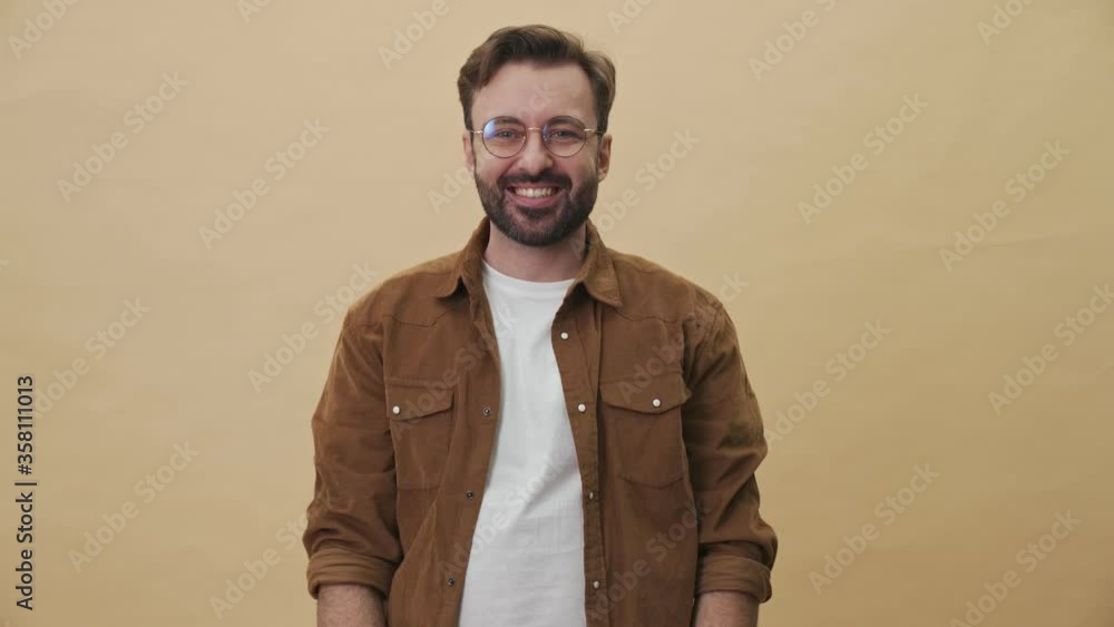 Sticker a happy smiling young unshaved man is doing winner gesture standing isolated over beige wall backgro