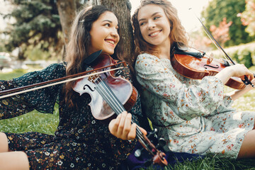 Girls in a summer park. Two ladies with a violin. Friends sitting on a grass