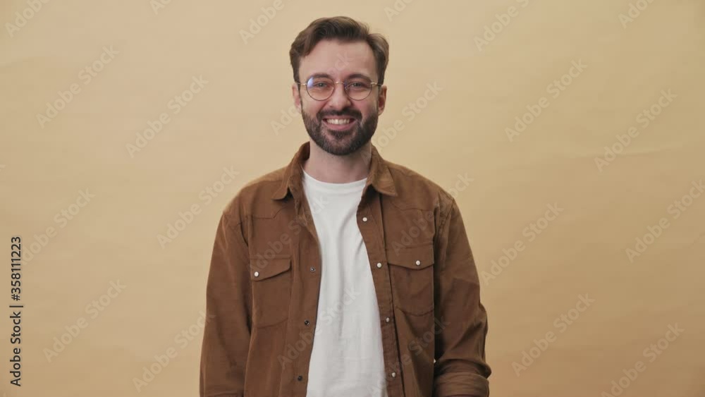 Sticker A pleased young unshaven man is raising his fingers up showing the copy-space standing isolated over beige wall background in studio