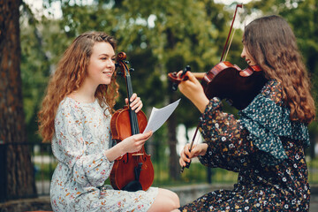 Girls in a summer park. Two ladies with a violin. Friends sitting on a bench