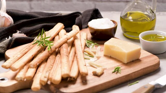 Fresh baked homemade grissini bread sticks in vintage metal grid box with olive oil and rosemary herbs over kitchen counter top.
