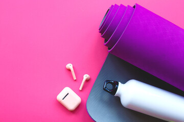 purple yoga mat, water bottle and headphones on a pink background