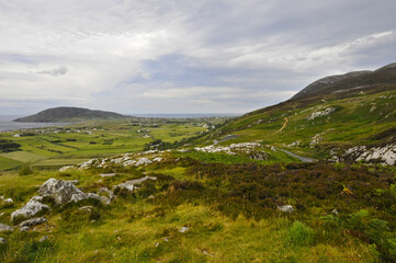 Vue panoramique sur la côte nord irlandaise, ses champs, ses collines, ses rochers et son ciel nuageux, depuis une route au sommet d'un col.