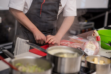 Chef chops meat and prepares meal beside boiling pans