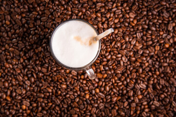 Coffee latte with frothy milk in tall glass, on coffee beans.