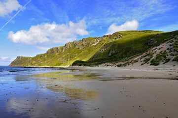 Dunes de sable et herbe verdoyante sur une plage du littoral au nord de l'Irlande. Ciel bleu et nuages blancs contrastant avec les couleurs des falaises.