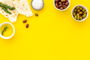 Top view of olives, olive oil, bread on yellow table top view copy space