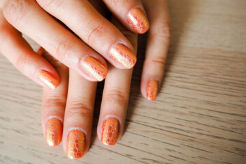 female hands with orange manicure in the form of snake skin on a brown background