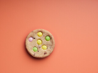 top view of a single cookie with colored candy embedded on top of an orange surface