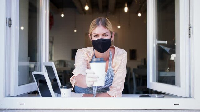 Woman with face mask serving coffee through window, shop open after lockdown.