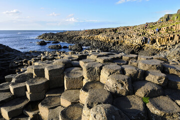 Vue sur les colonnes basaltiques hexagonales, la mer bleue et les gens marchant sur la chaussée des géants, cette zone géologique volcanique du nord de l'irlande.