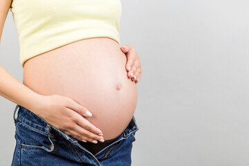 Close up of pregnant woman in unzipped jeans showing her naked belly at colorful background with copy space. Baby expecting concept