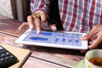 man's hand working on digital tablet at office desk, using self created chart 