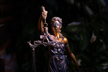 Themis statue, concept of law and justice on the background of a green flowerpot. Close up.
