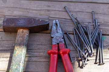 Old construction tools, nails, a hammer and pliers with red handles lie on a plank wooden floor. A game of shadow and light. Repair, construction, carpentry workshop. Close-up, a group of objects.