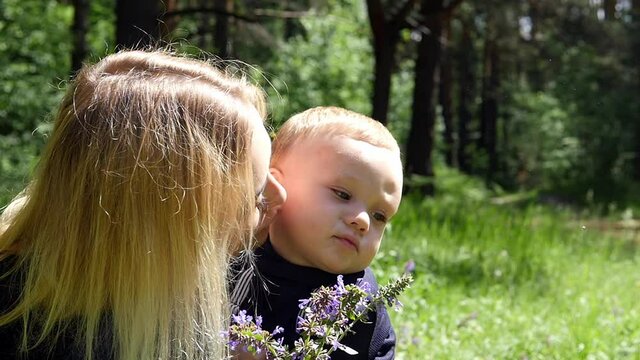 Blond cheerful boy next to mom watches butterflies on the green grass.