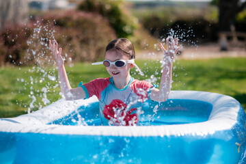 Little girl has fun splashing in paddling pool in summer