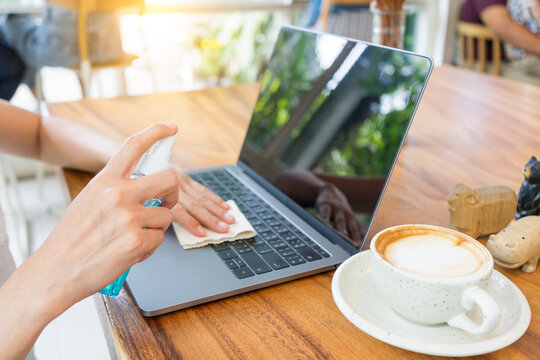 A hand female spraying and wiping cleaning laptop keyboard at cafe working space.  Prevention COVID 19, coronavirus, Safety sanitation concept