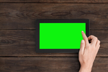 Presses the index finger on the tablet with a green screen. Top view on a dark brown wooden table.