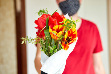 Courier, delivery man in red in gloves safely delivers online purchases a bouquet of flower during coronavirus epidemic. Stay home, safe concept. Contactless delivery service under quarantine. .