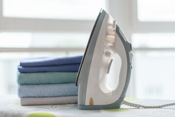 Electrical iron and clean clothes on a ironing board background.