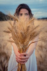 Young girl holding a grain of wheat in a field in her hands