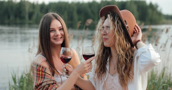 two cute lesbians on the background of a lake drinking wine on the bruderschaft
